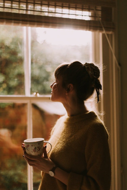 Γυναίκα με κούπα στο χέρι που κοιτάει έξω από το παράθυρο 